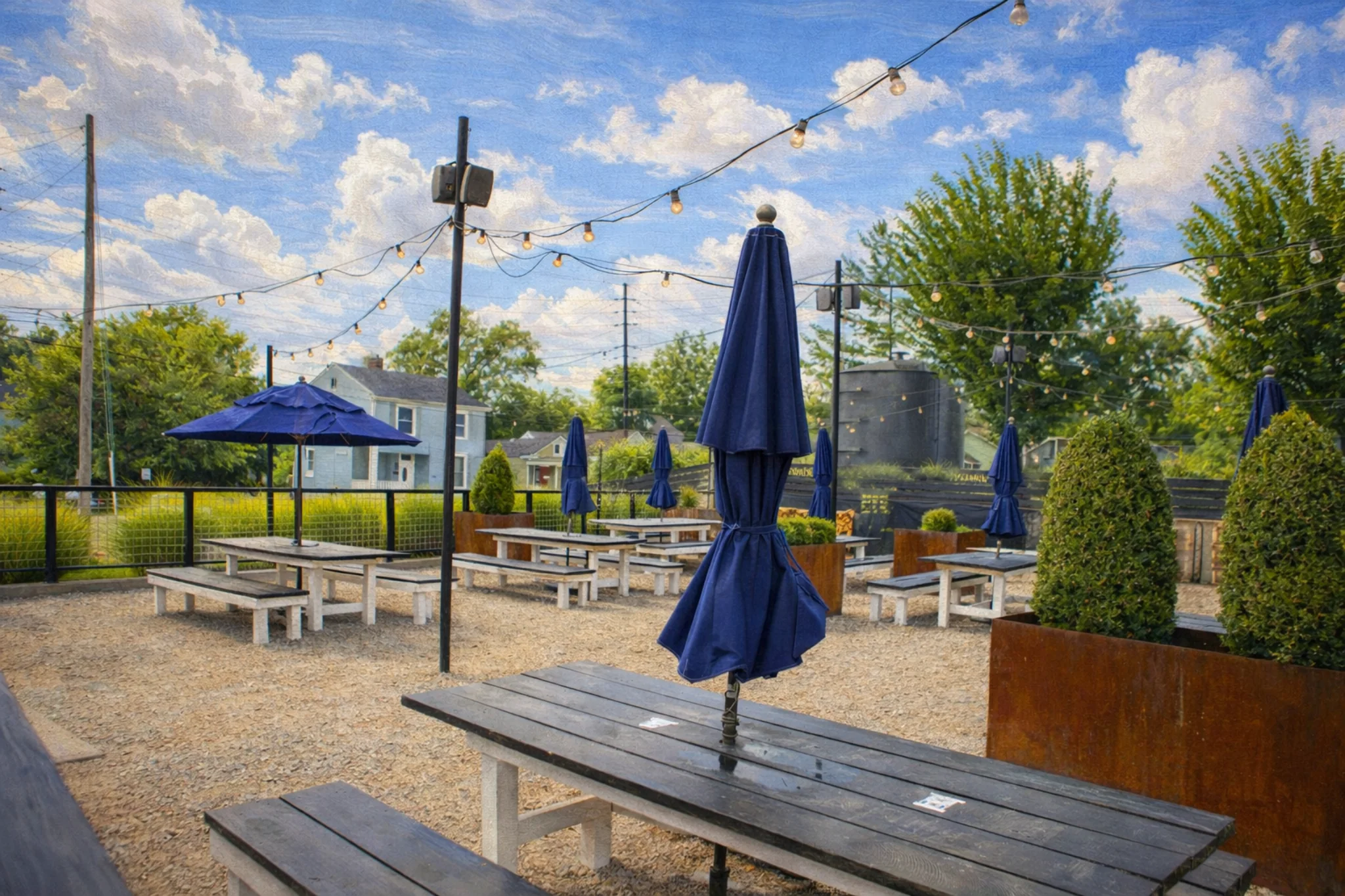 Hop Atomica outdoor patio in Louisville, Kentucky with picnic tables, blue umbrellas, and string lights.
