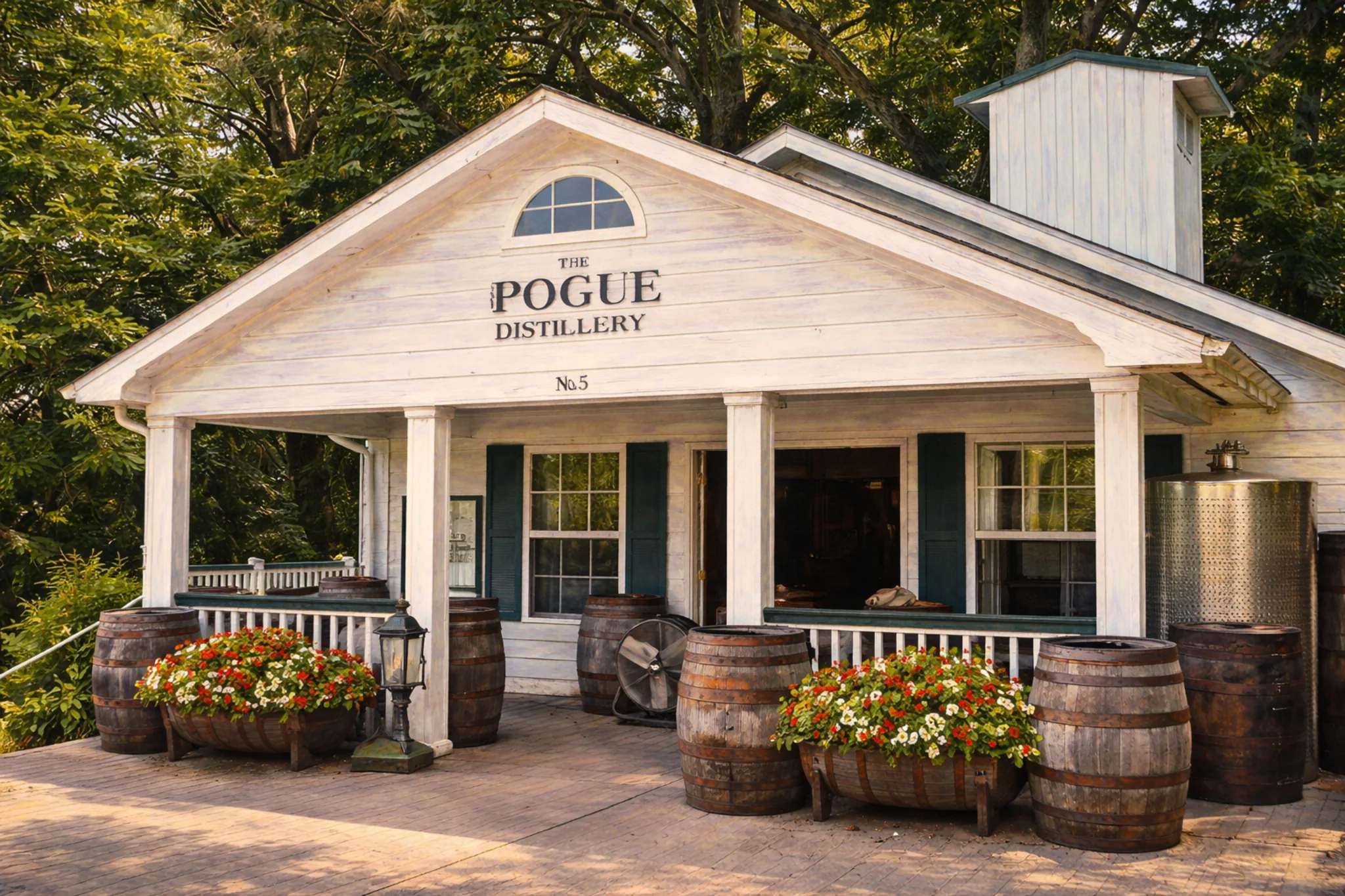 Front porch of Old Pogue Distillery with “The Pogue Distillery” sign, bourbon barrels, and flower planters.