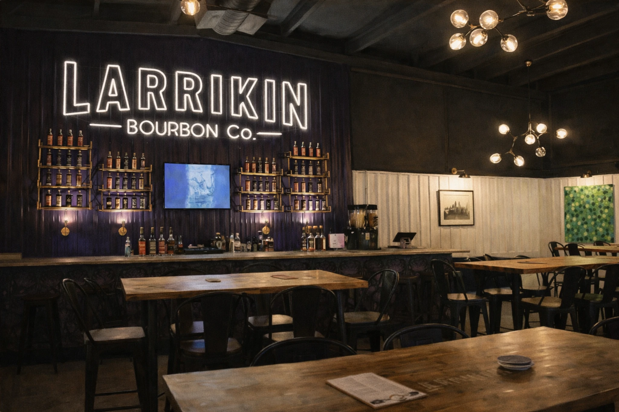 Wide view of Larrikin Bourbon Company tasting room with tables, bar seating, and glowing signage.