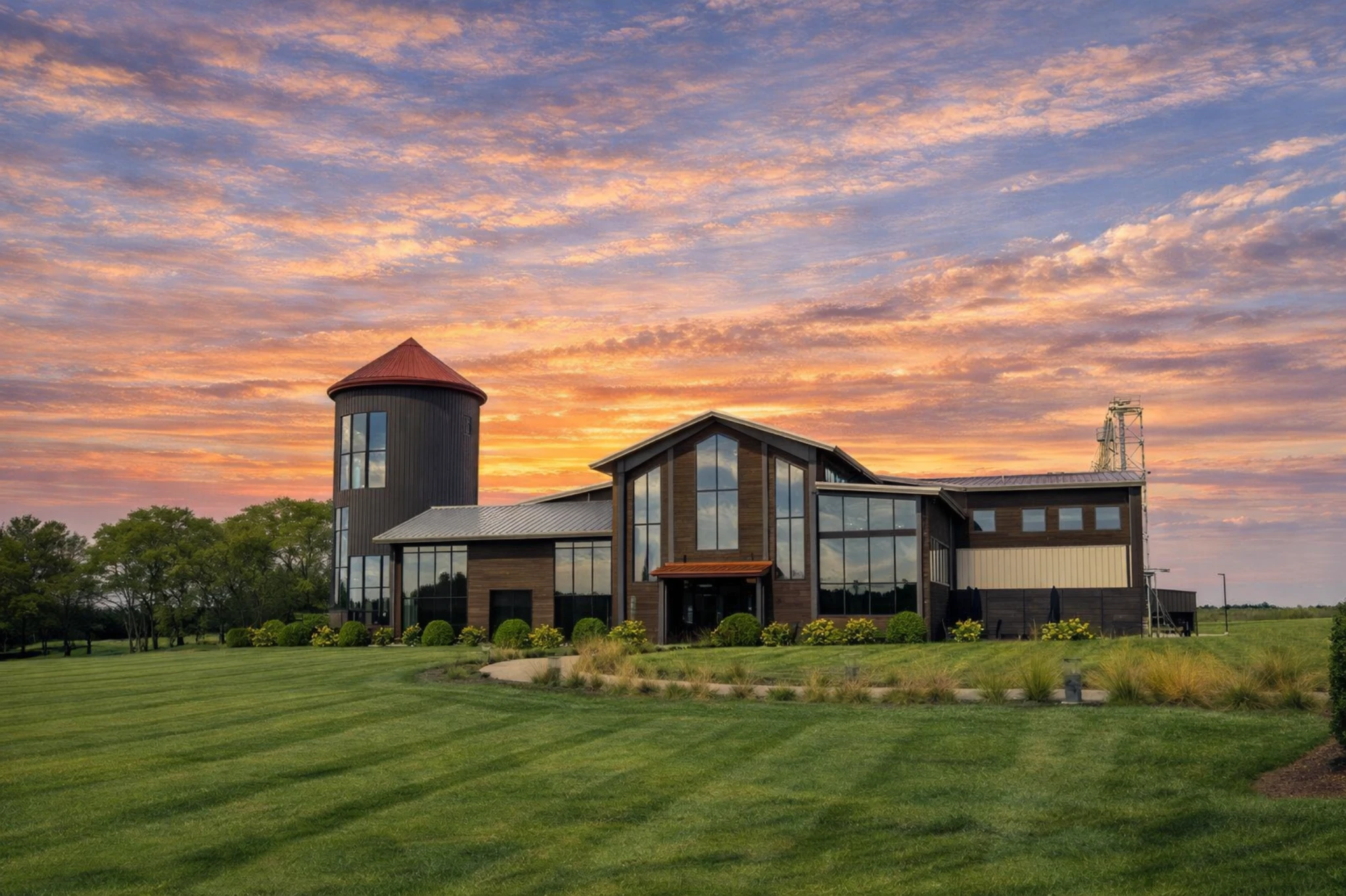 Exterior of Lux Row Distillers main building with glass facade and silo tower at sunset.