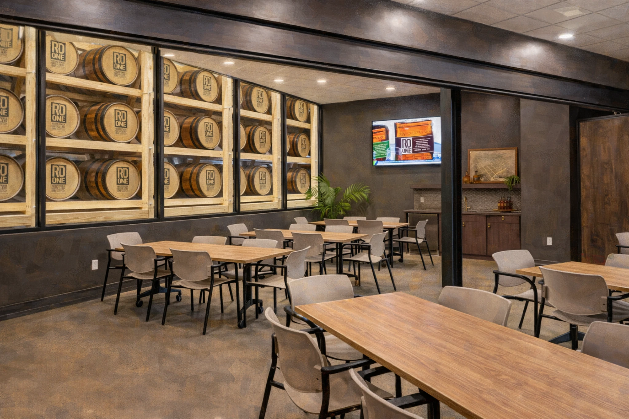 RD1 Spirits Distillery tasting room featuring wood tables, modern seating, and a glass wall displaying stacked RD1 bourbon barrels.