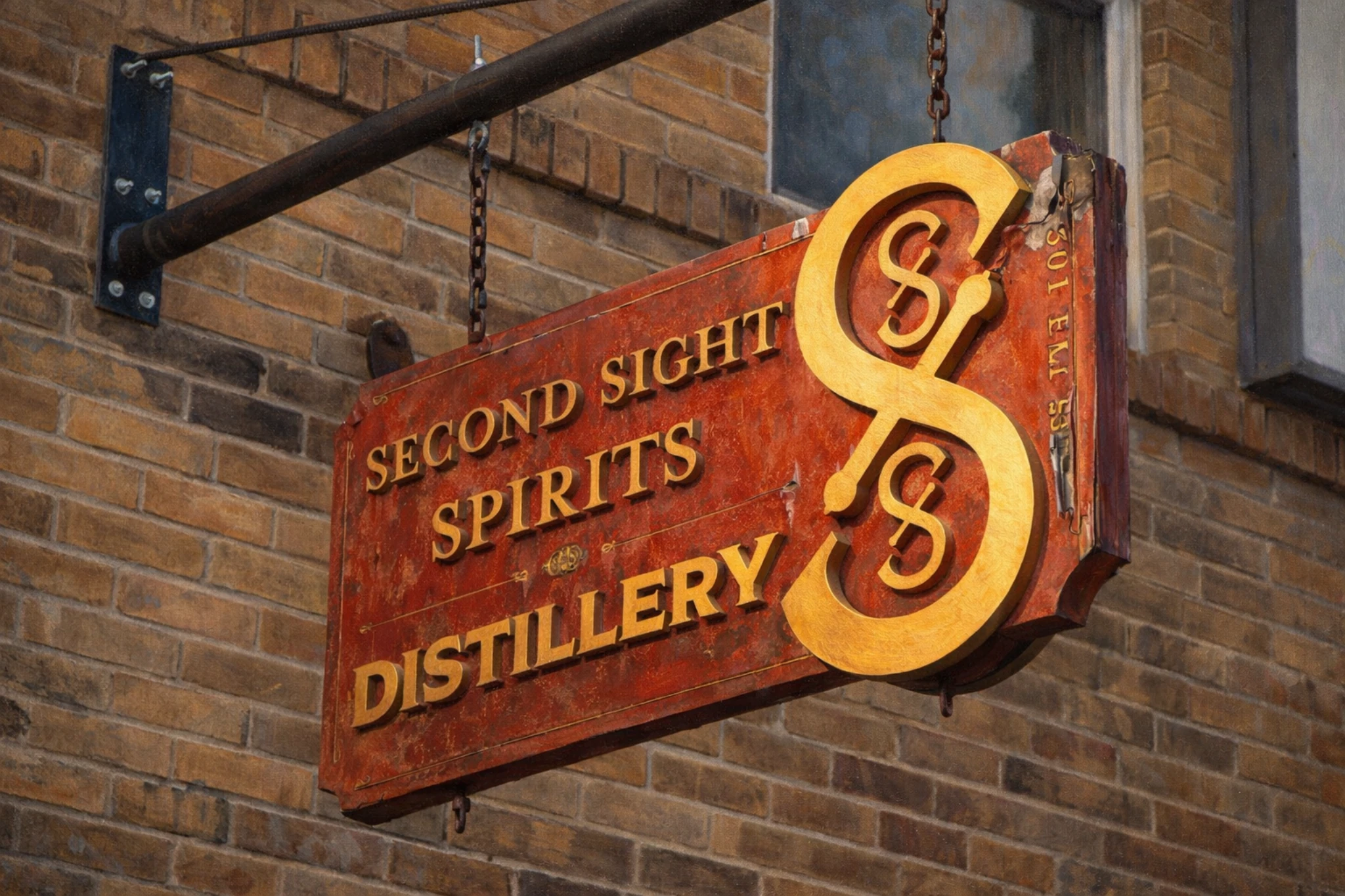 Hanging exterior sign for Second Sight Spirits Distillery mounted on a brick building, featuring a stylized gold logo and lettering.