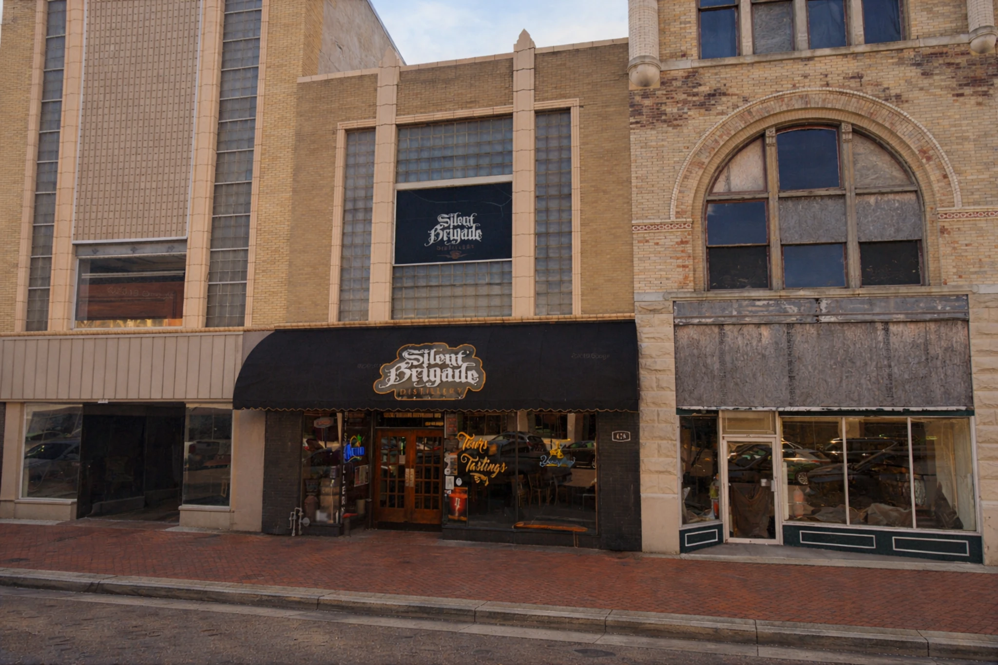 Downtown storefront exterior of Silent Brigade Distillery with a black awning, brick façade, and street-level entrance in a historic building.