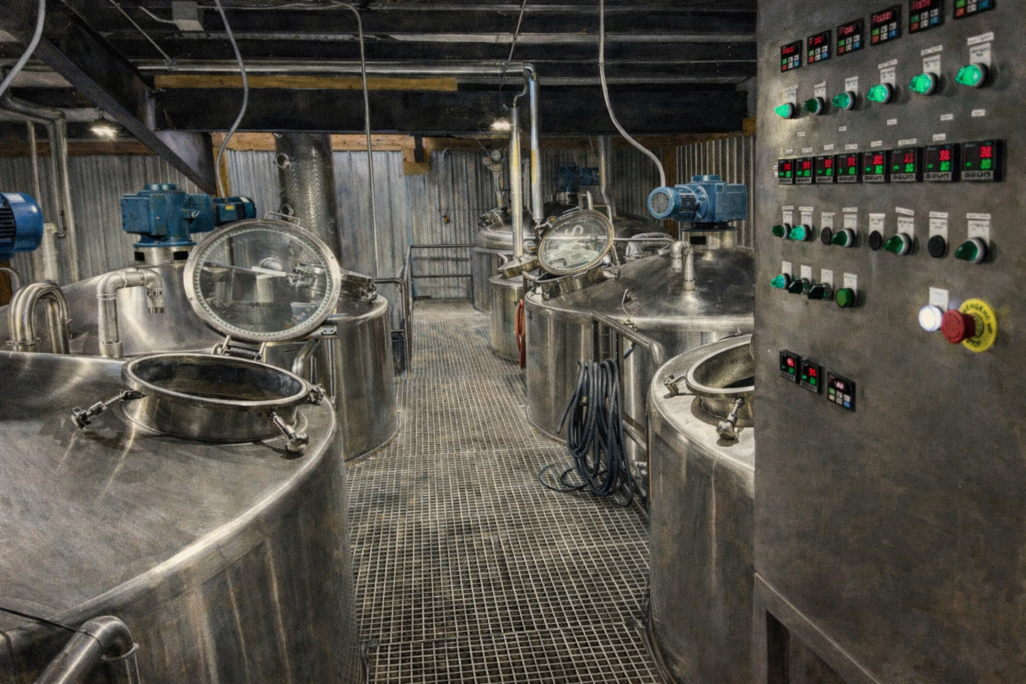 Fermentation room inside Southern Kentucky Distillery featuring stainless steel tanks, a grated walkway, and a control panel with digital readouts and switches.