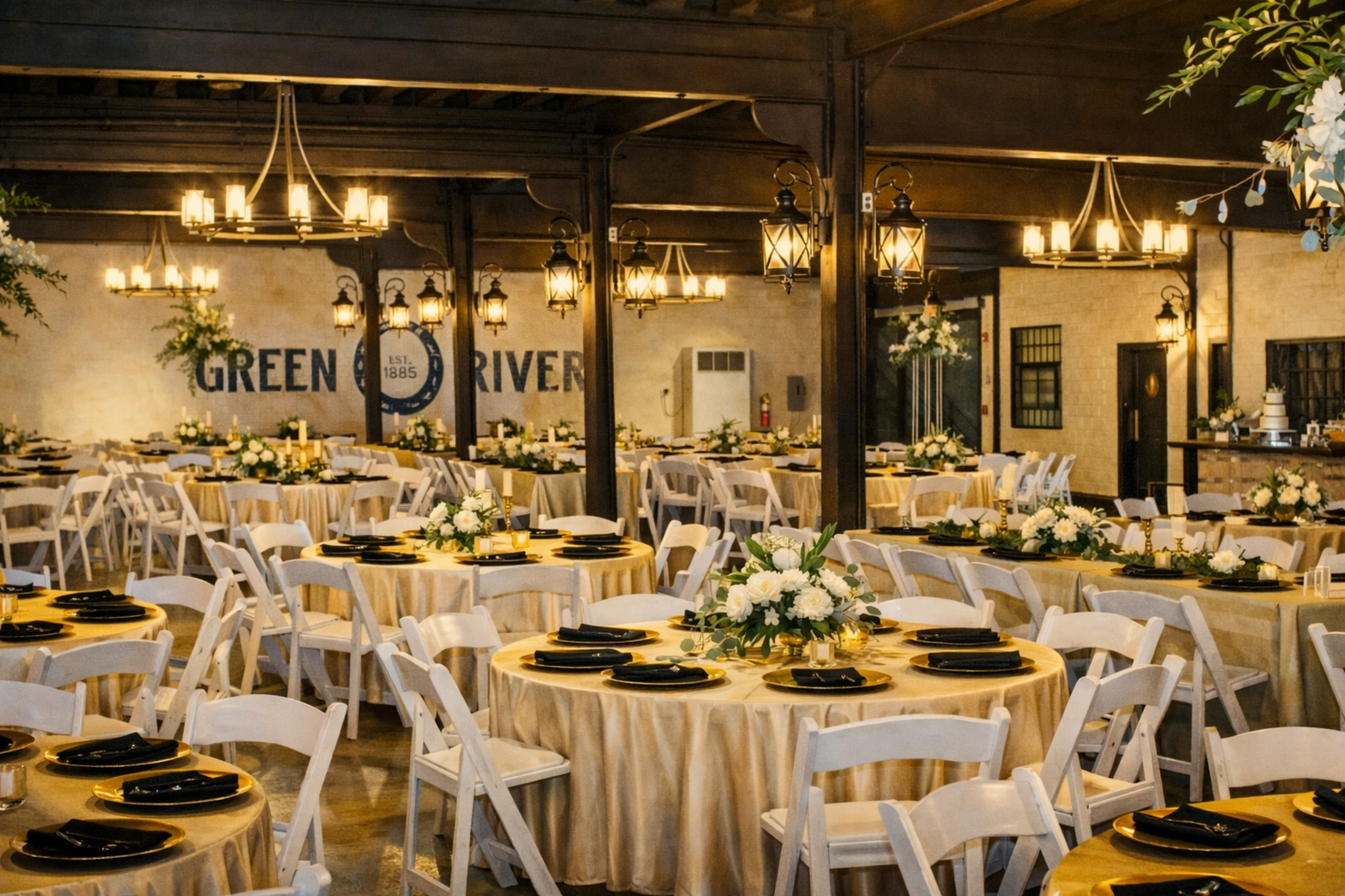 Event space at Green River Distilling Co. in Owensboro, Kentucky, with round banquet tables, floral centerpieces, white chairs, and warm lantern lighting.