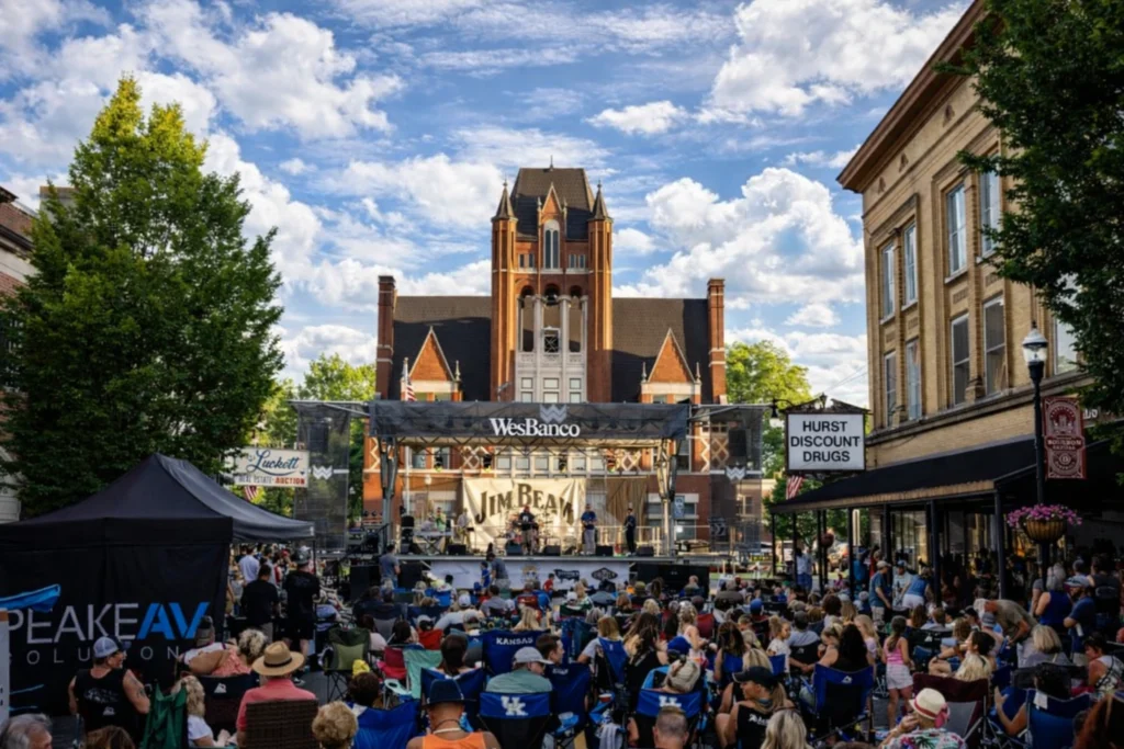 Crowd gathered in downtown Bardstown for a National Bourbon Week concert with a stage set in front of a historic church.